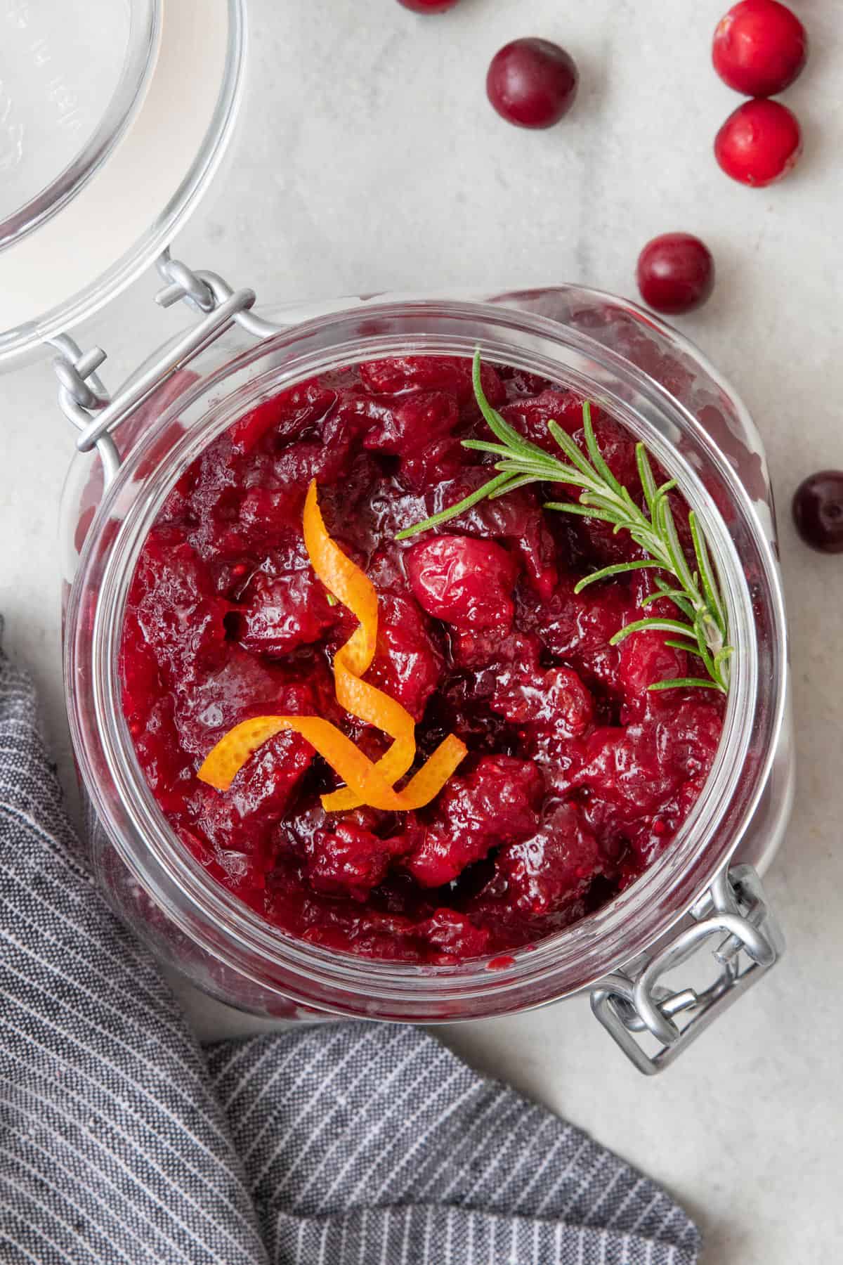 Final cranberry orange sauce in a glass jar with orange zest and fresh herb.