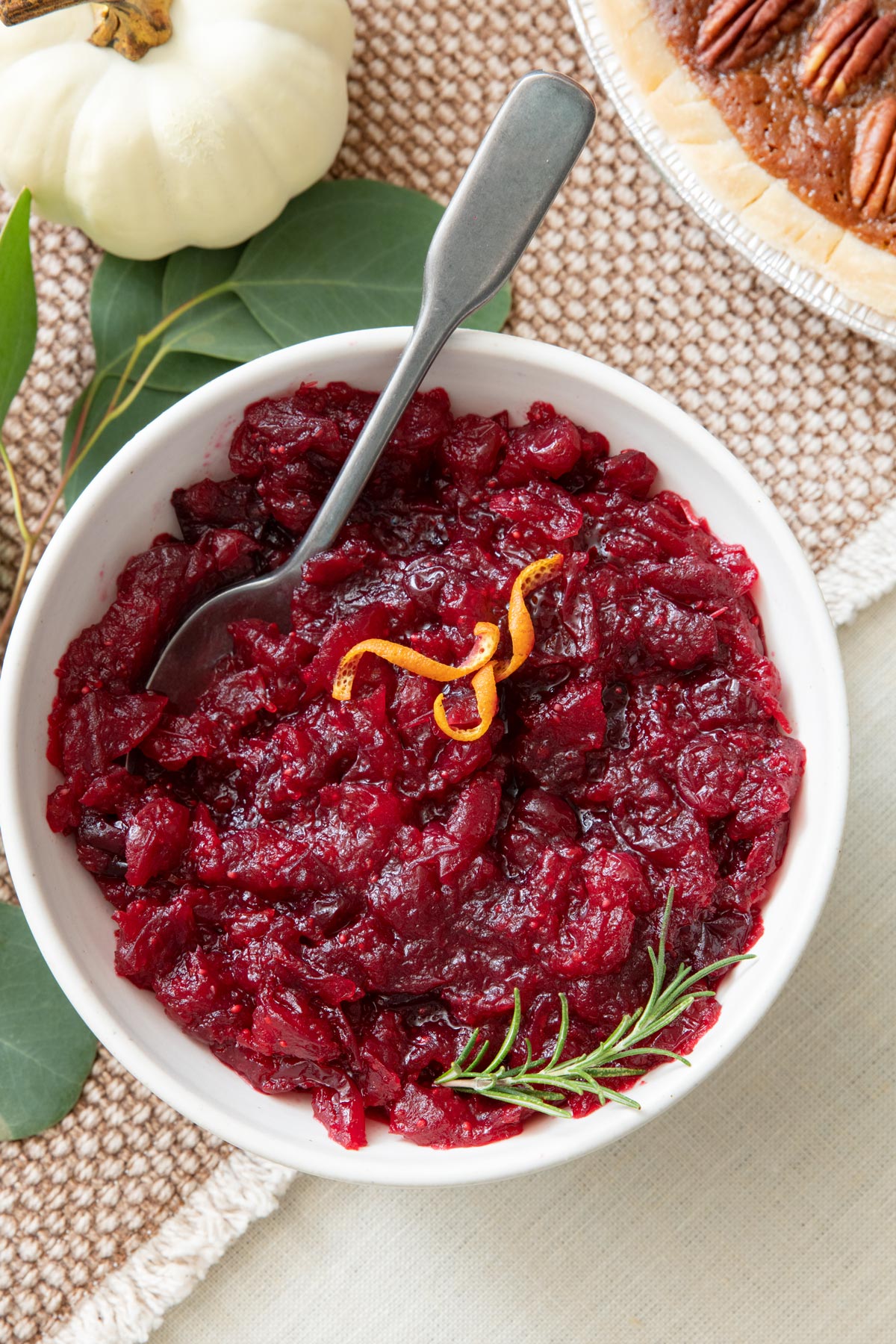 Bowl of cranberry orange sauce garnished with orange zest and fresh sprig of thyme with a spoon dipped in.
