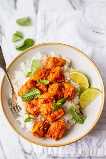 Final plated harissa chicken served over rice with lime wedges and mint leaves