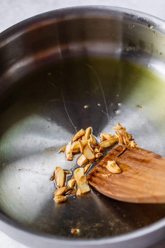 Stainless steel pan with a wooden spatula frying sliced garlic