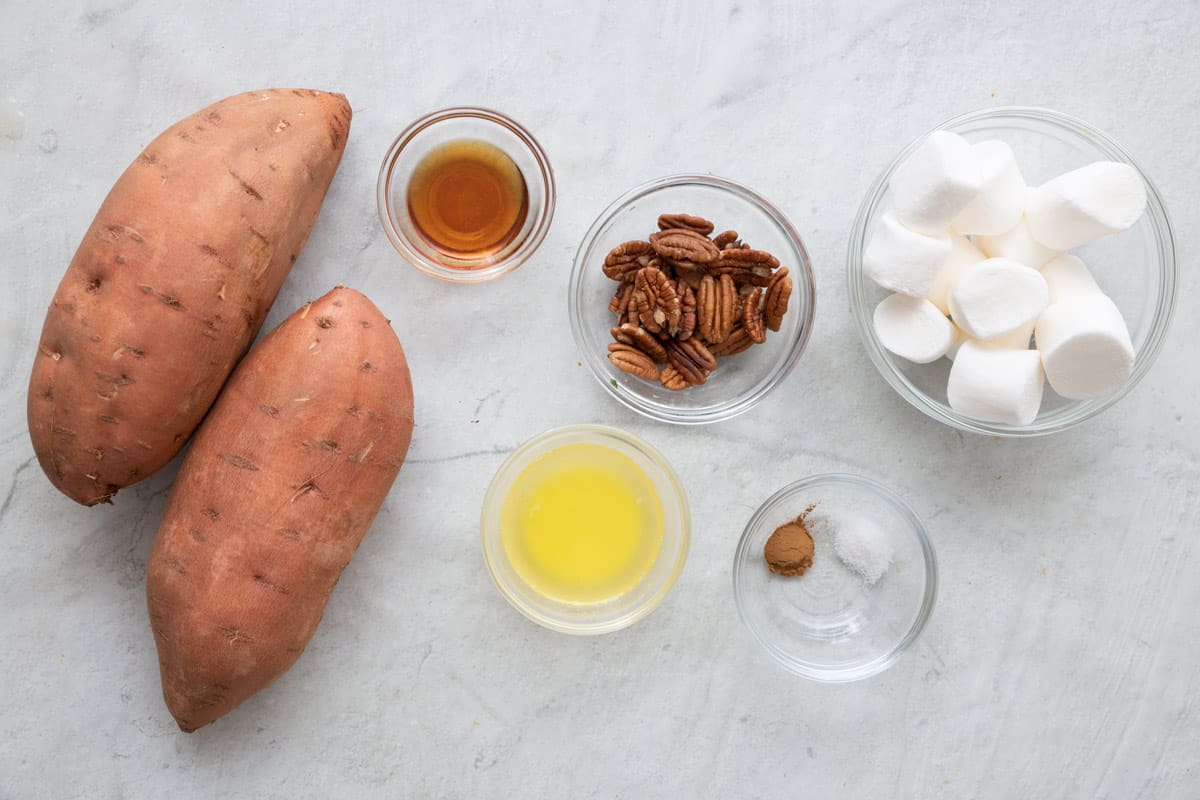 Ingredients for recipe before prepped in individual bowls: 2 large sweet potatoes, maple syrup, melted butter, pecan halves, cinnamon and salt, and marshmellows.