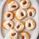 Sweet potato bites on a oval white dish with melted marshmallows and a pecan half on each with a spatula lifting one up.
