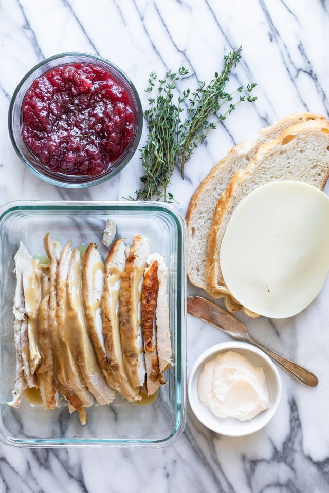 Marble background with sourdough slice bread, cheese, turkey, cranberry sauce, thyme, and mayonnaise