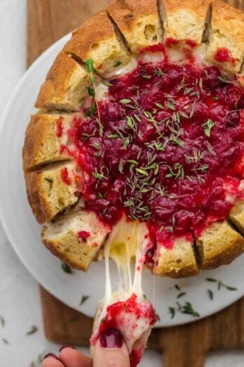 Baked brie cranberry in bread bowl after baked. Slice of bread being pulled away