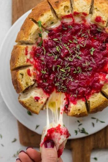 Baked brie cranberry in bread bowl after baked. Slice of bread being pulled away