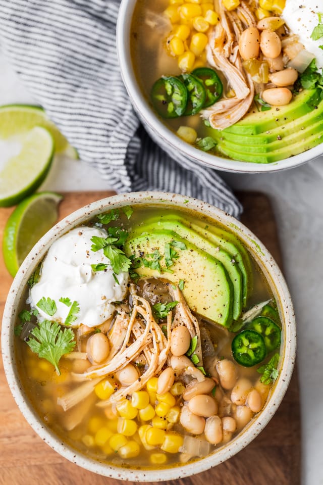 Two bowls of easy white chicken chili with toppings: avocado, sour cream, jalapenos, cilantro