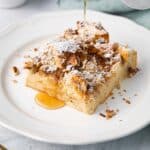 Close up shot of slice of easy french toast casserole with maple syrup getting poured on top.