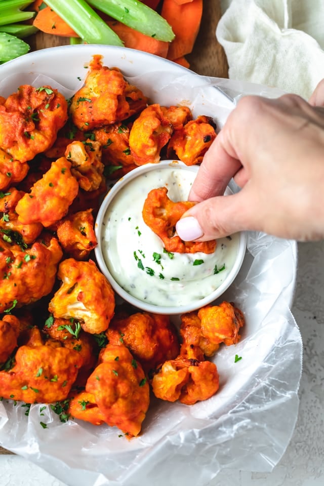 Large bowl of cauliflower buffalo bites with one bite getting dipped in ranch dressing