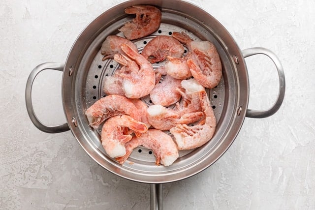 Getting ready to steam shrimp in a steamer over a pot of boiling water