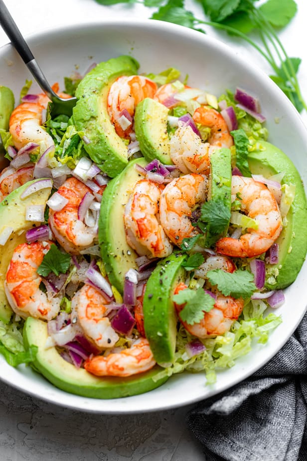 Serving shrimp avocado salad with a large spoon and fork