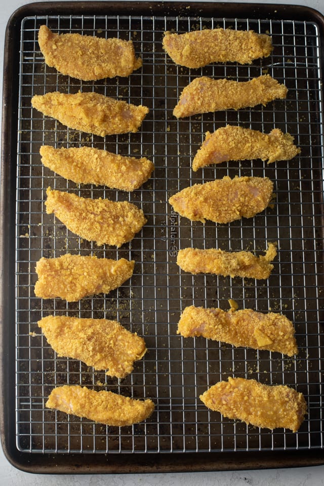 Tortilla crusted chicken on a wired rack over pan right before baking