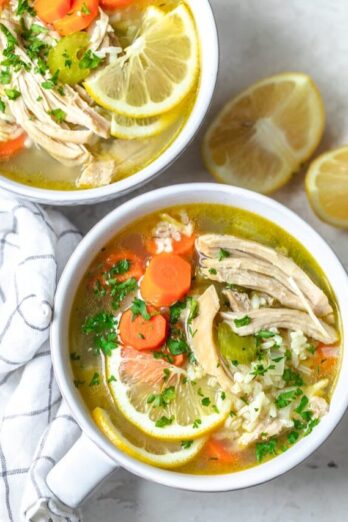 Two bowls of chicken lemon rice soup on a counter with lemons