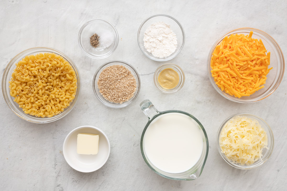 Ingredients for recipe in individual bowls: dry macaroni, salt and pepper, breadcrumbs, butter, flour, dijon, milk, shredded cheddar, and shredded gruyere cheese.