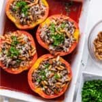 Baking dish with stuffed peppers, topped with pine nuts adn parsley