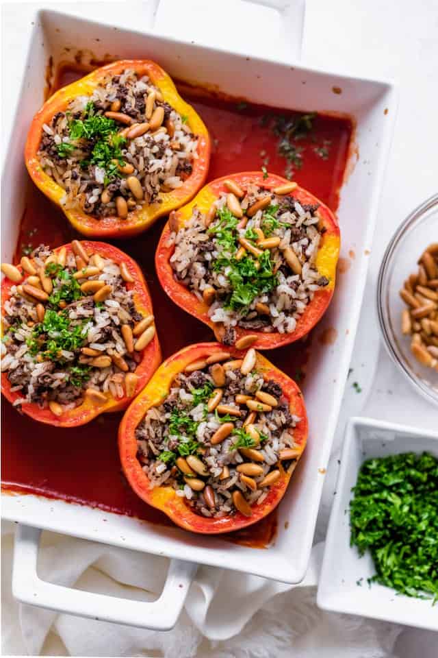 Baking dish with stuffed peppers, topped with pine nuts adn parsley