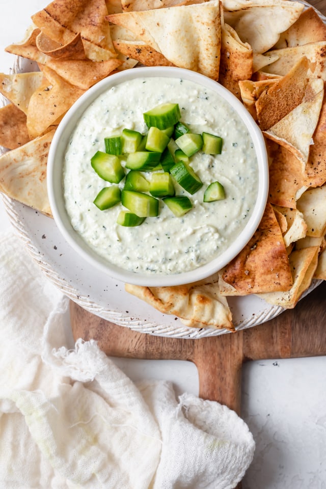Creamy feta dip in a small bowl topped with cucumbers served with pita chips