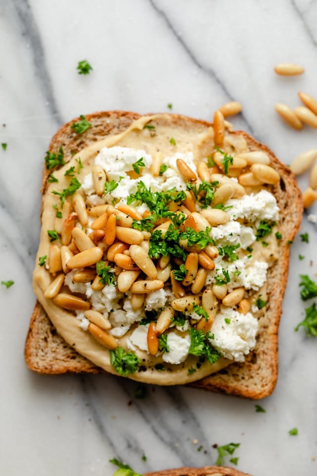 Hummus toast made with feta cheese, toasted pine nuts and parsley