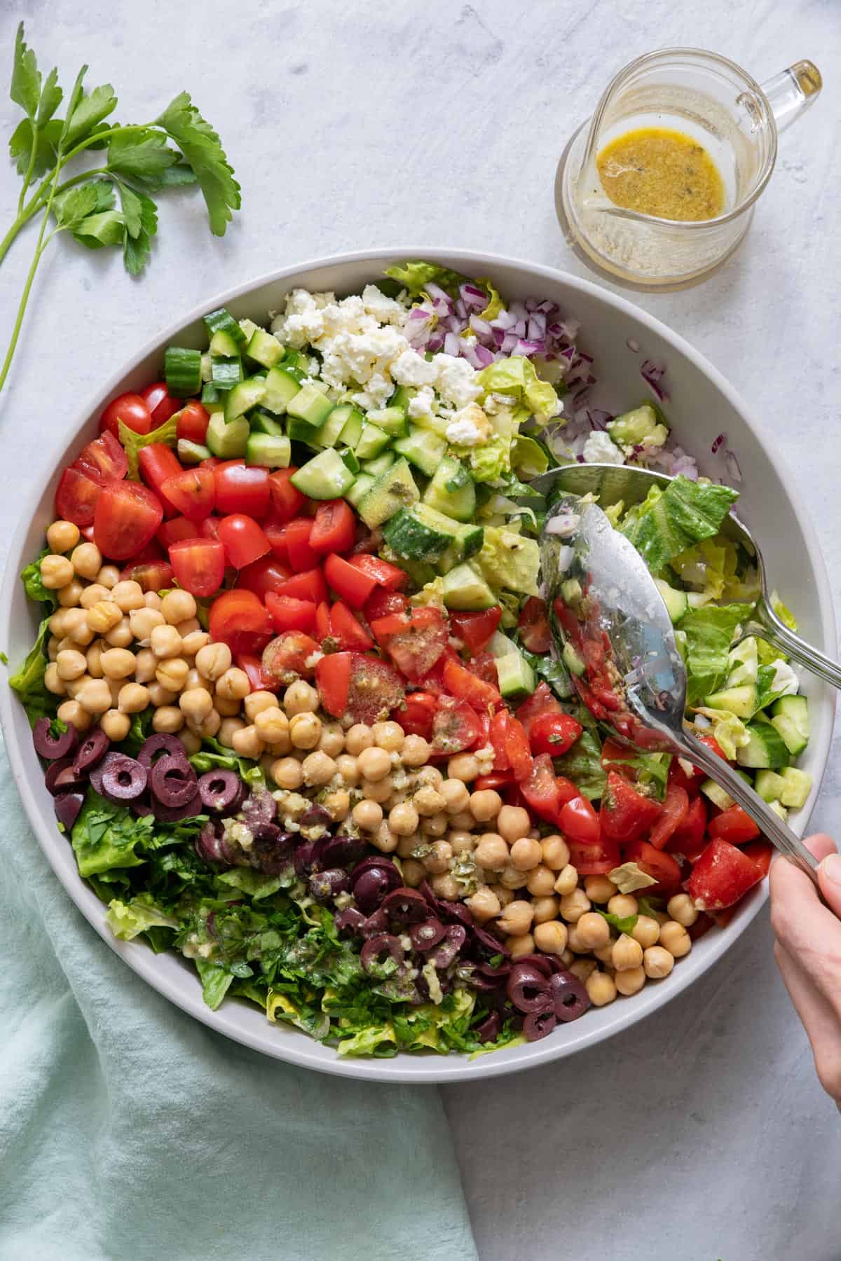 Two spoons scoop a serving of Mediterranean Chopped salad from a large serving dish.
