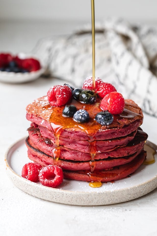 Pink pancakes stack topped with berries and maple syrup