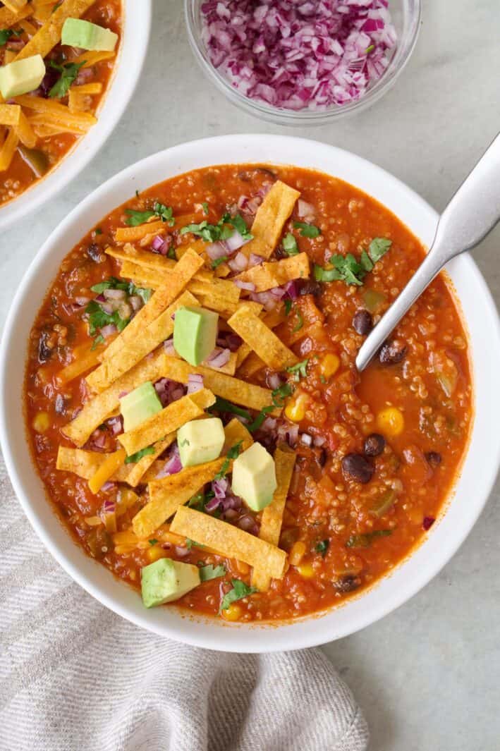 Vegetarian quinoa tortilla soup with crunchy tortilla strips on top and a spoon dipped in.