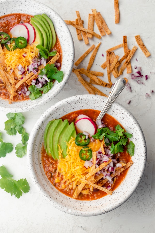 Two bowls of vegetarian tortilla soup topped with cheese, onions, avocado and tortilla chips