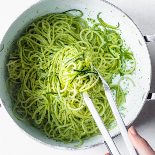 Spaghetti and zoodles getting tossed with pesto sauce