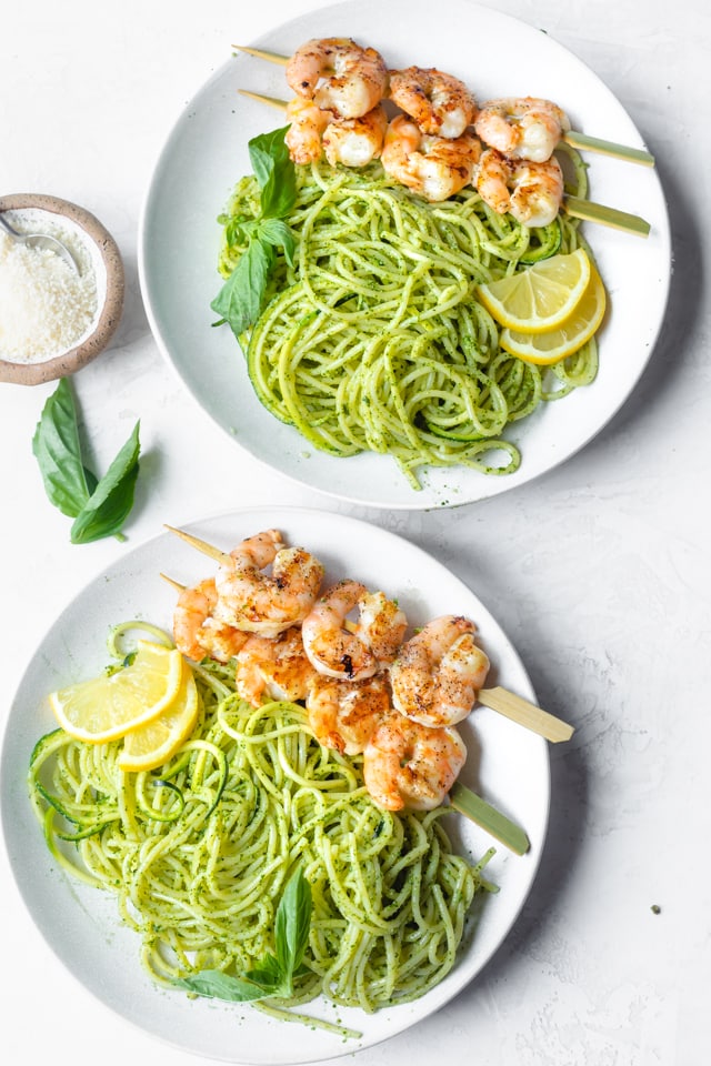Two plates of the pesto spaghetti with grilled shrimp on skewers