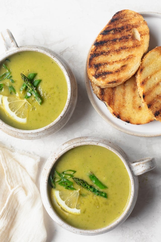 Final vegan asparagus soup in soup mugs served with grilled bread