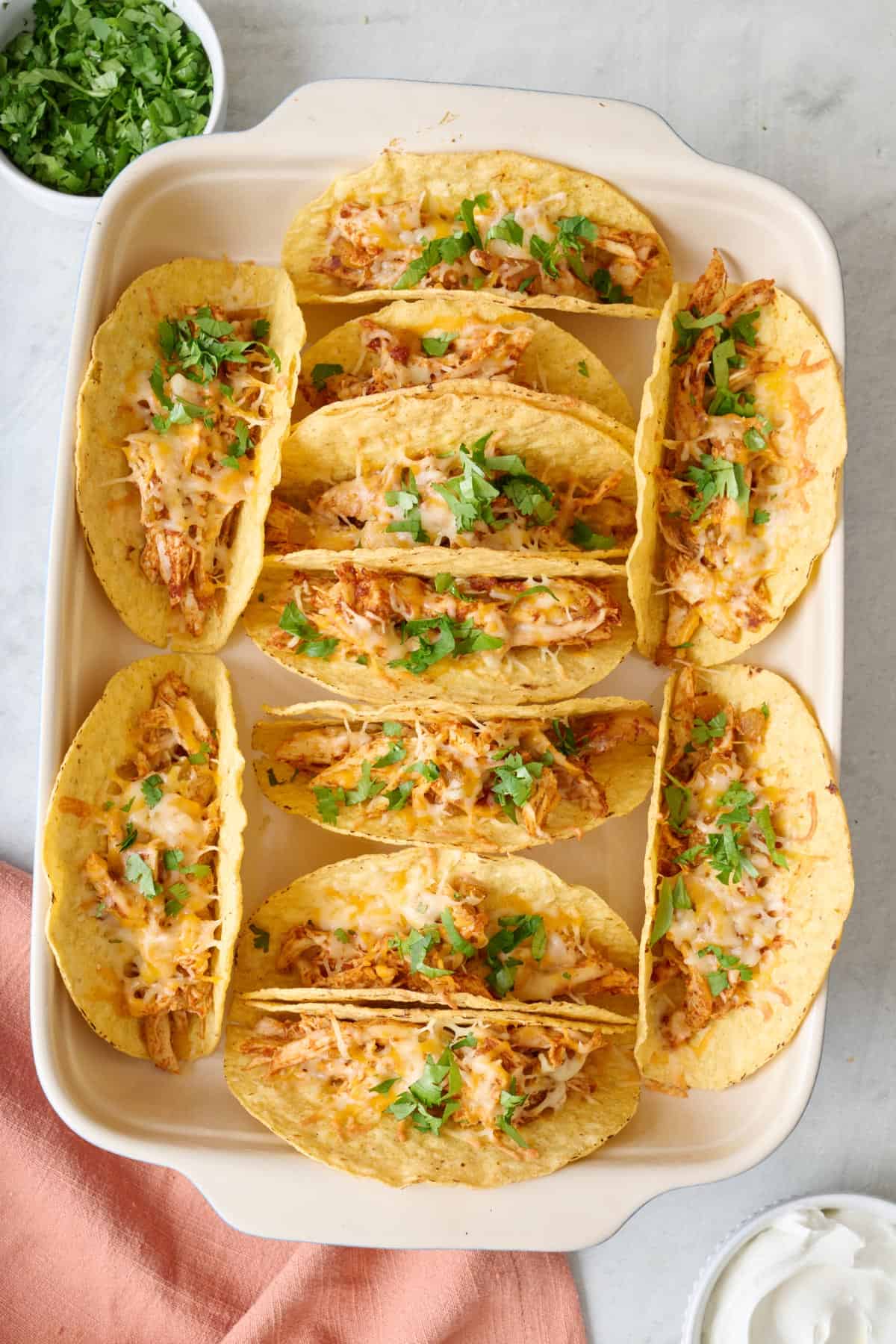 12 baked chicken tacos in a baking pan garnished with fresh cilantro.