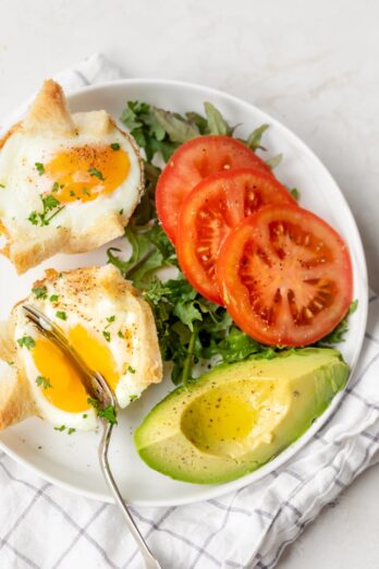 Cutting into eggs on a plate with tomatoes and vocado