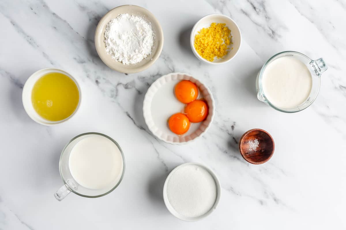 Ingredients for recipe in individual bowls: lemon juice, lemon zest, cornstarch, milk, heavy cream, egg yolks, and salt.