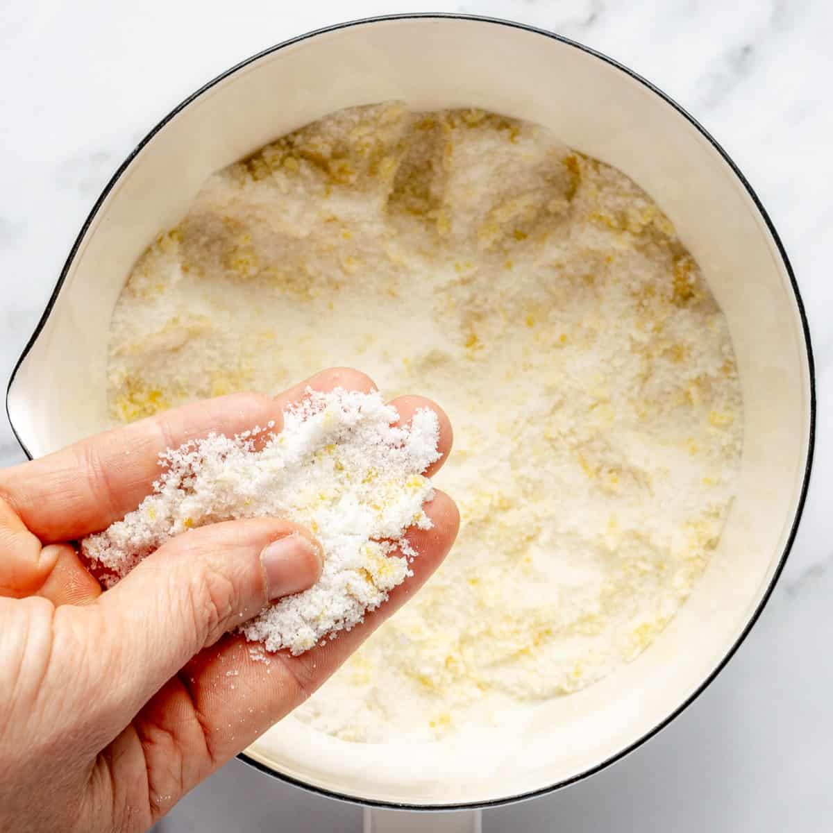 Sugar and lemon zest in a bowl with fingers massaging them together