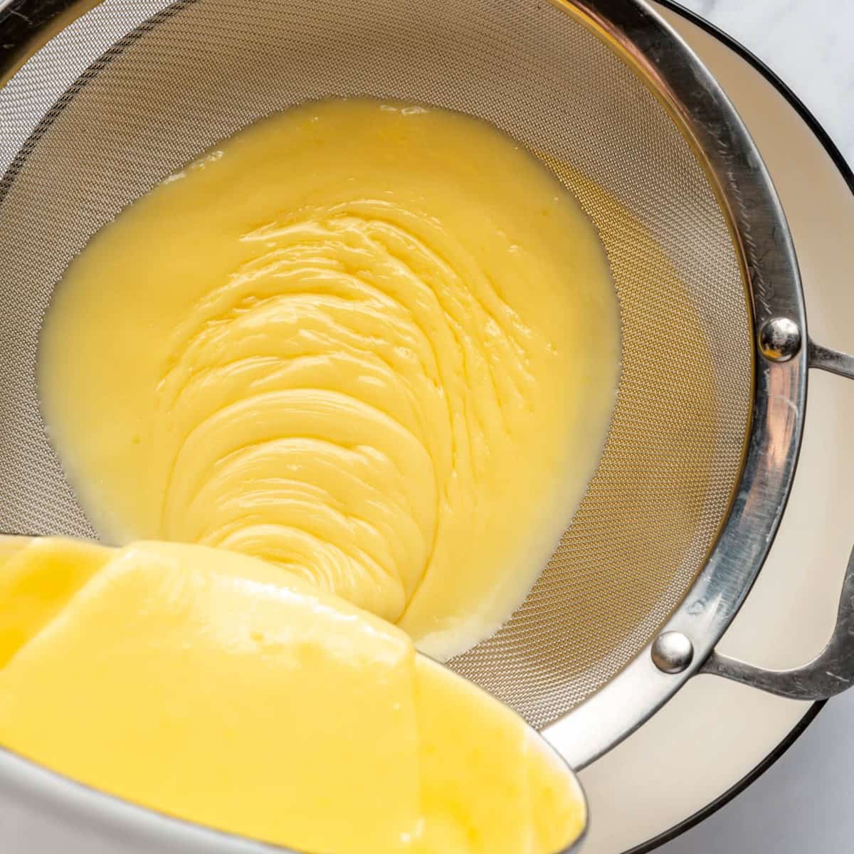 Pouring cooked pudding through a fine mesh sieve.