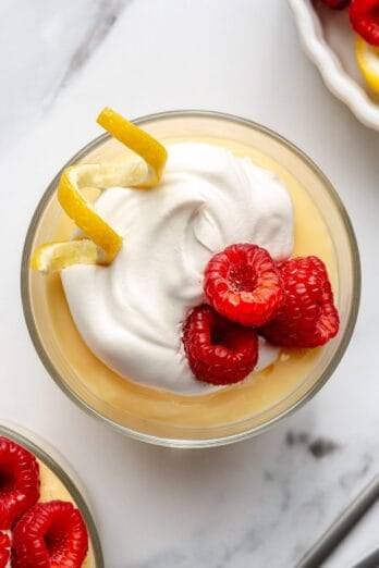 Homemade lemon pudding topped with whipped cream, fresh raspberries, and lemon zest.