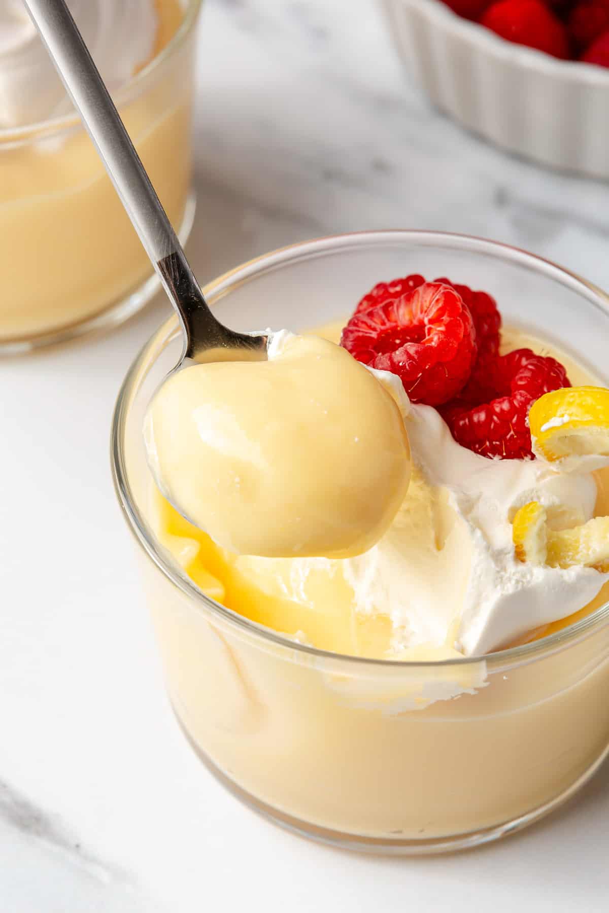 Spoon lifting up a bite of lemon pudding from a small dish to show smooth and creamy texture.