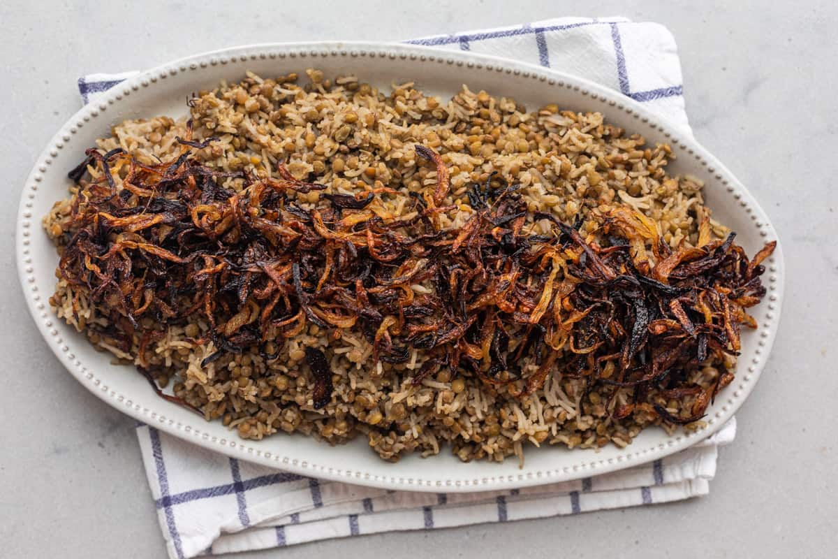 Cooked lentils and rice on a large platter with crispy onions on top.