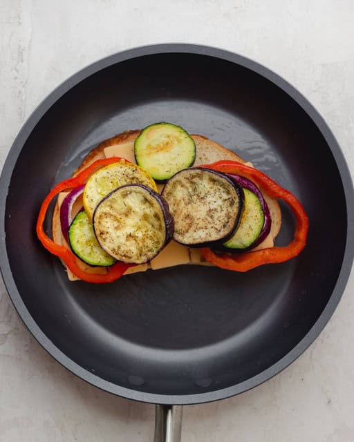 Slice of bread in a pan, with a layer of cheese and roasted veggies.