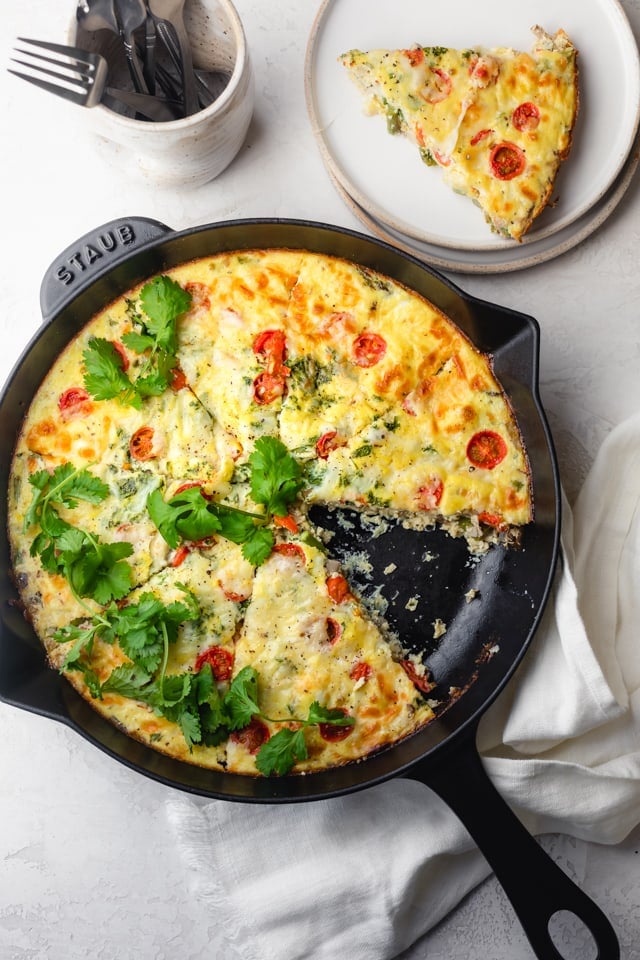 Vegetable frittata in a cast iron pan with one slice removed for serving