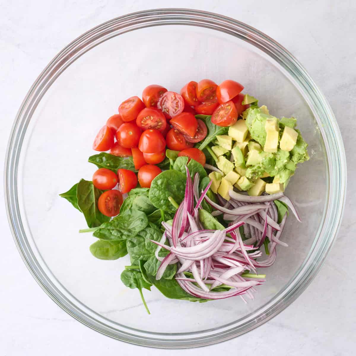 Cherry tomatoes, baby spinach, diced avocado, and red onion in a large bowl before combining.