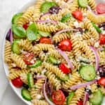 Final Greek Pasta Salad recipe in a large bowl with cucumbers, tomatoes, onions, olives and feta cheese