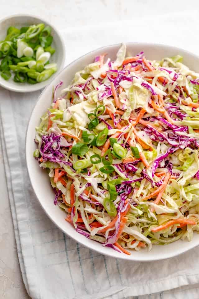 Healthy Coleslaw in a large bowl on a white napkin with green onions on the side