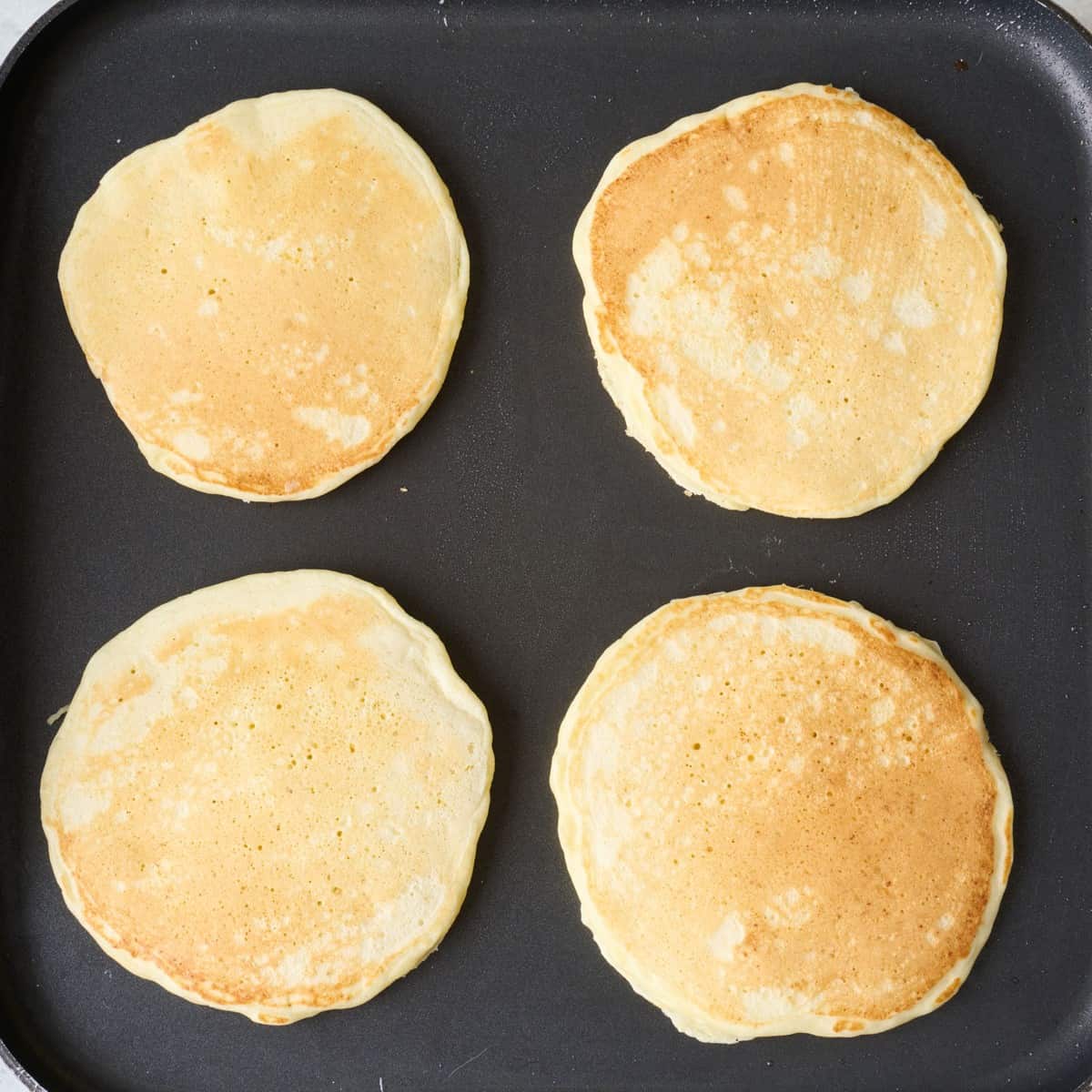 4 pancakes on a griddle after flipping.