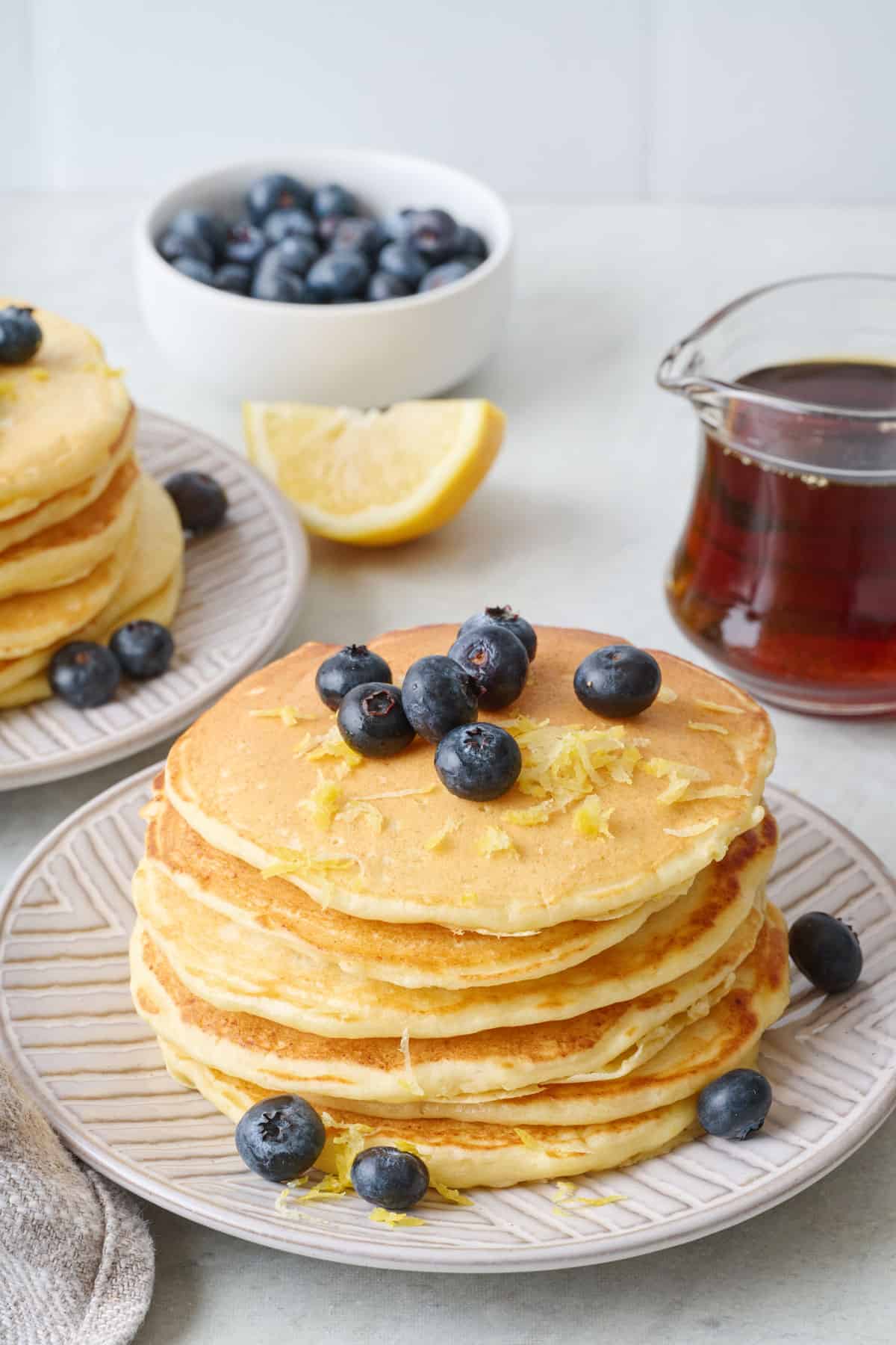 Stack of lemon ricotta pancakes with lemon zest and fresh blueberries on top.