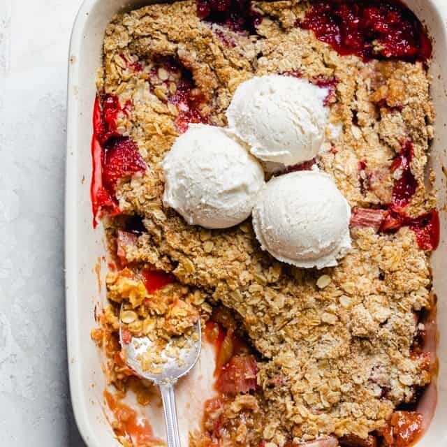 Final rhubarb crisp with scoop taken out and ice cream scoops on top of baking dish