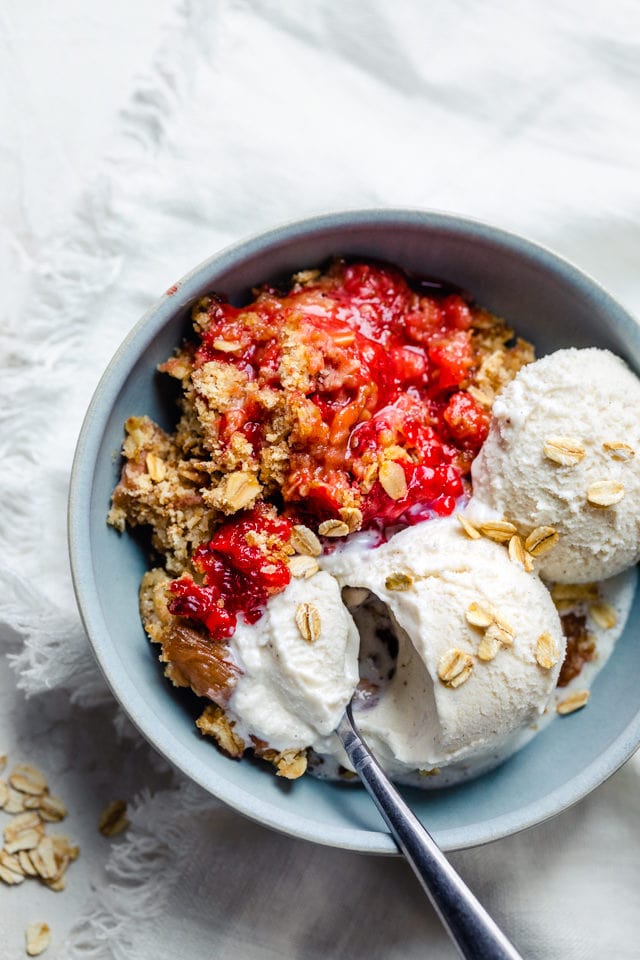 Strawberry rhubarb crisp recipe in a bowl with two scoops of ice cream and a spoon in the bowl