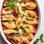 Cheese stuffed shells in a white oval baking dish topped with fresh basil