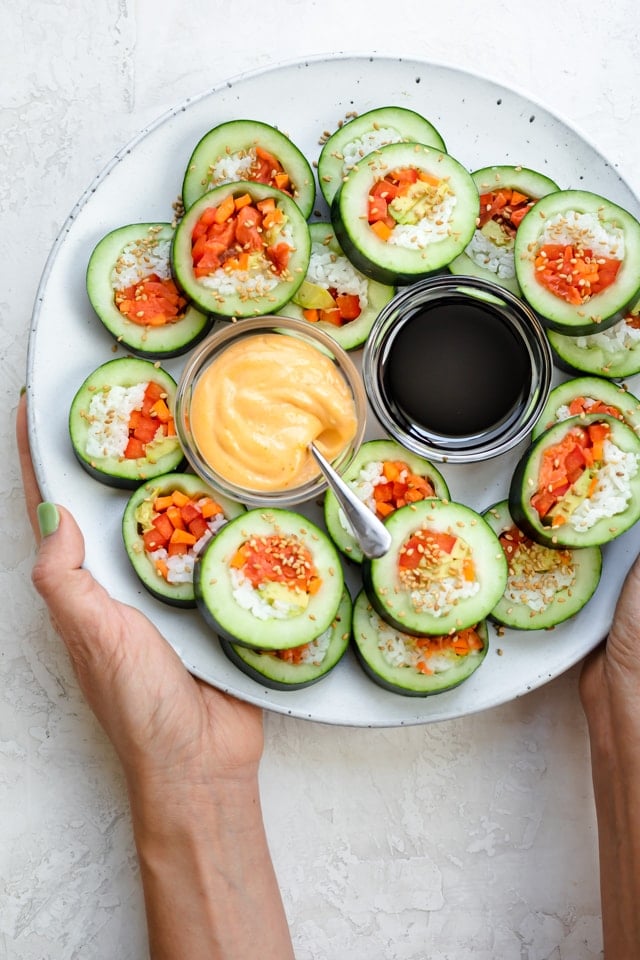 Two hands serving a large plate of cucumber sushi