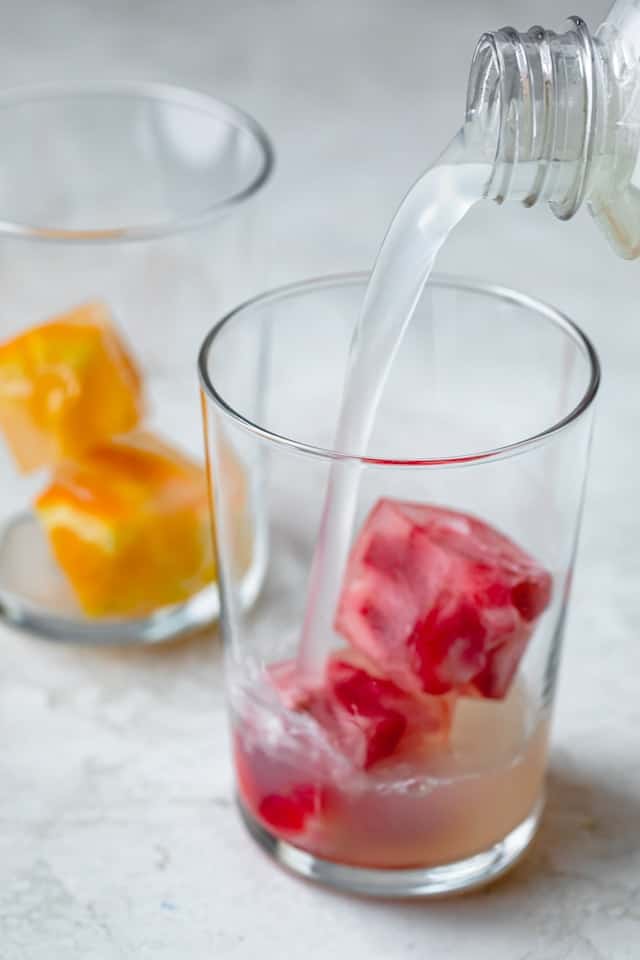 Pouring limeade into a cup with fruit cubes