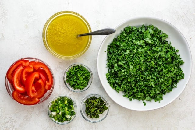 Ingredients to make the recipe: chopped kale, chopped parsley, chopped mint, chopped green onions, seeded slices of Roma tomatoes and a lemon/olive oil/bulgur mixture