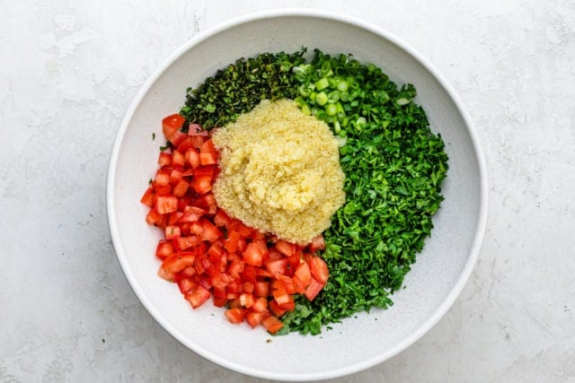 Large white bow with kale, parsley, mint, green onions and tomatoes topped with the olive oil/lemon juice/bulgur mixture